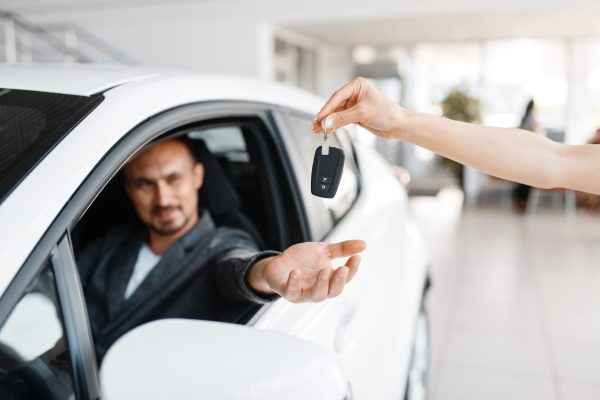 Happy man takes the key to new car in showroom Happy man takes the key to the new car in showroom. Male customer buying vehicle in dealership, automobile sale
