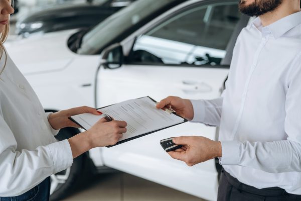 Signing up the document. Close up view of man and woman is dealership.