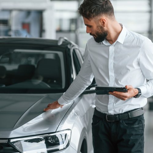 Touching the surface of automobile. Young man in white clothes is in the car dealership Touching the surface of automobile. Young man in white clothes is in the car dealership.