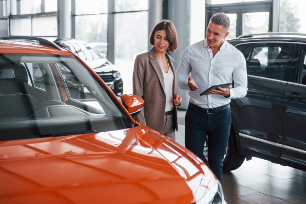 With notepad. Man in formal wear helping customer with choice of the automobile With notepad. Man in formal wear helping customer with choice of the automobile.